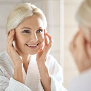Older woman looking at face wrinkles in the mirror